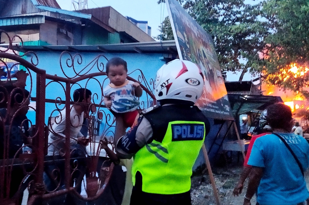 An Indonesian policeman helps evacuate a family as houses burn after hundreds of demonstrators marched near Papua's biggest city Jayapura on August 29, 2019. AFP / Indra Thamrin Hatta 