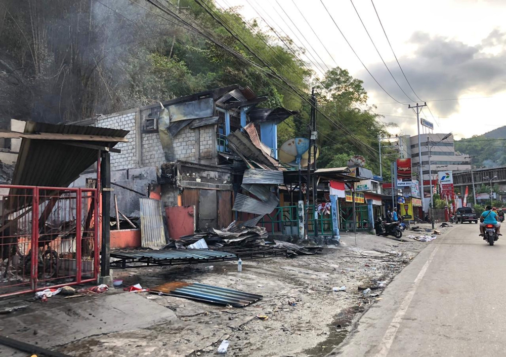 Residents ride motorcycles next to torched shops in Jayapura on August 30, 2019. AFP / BRAM