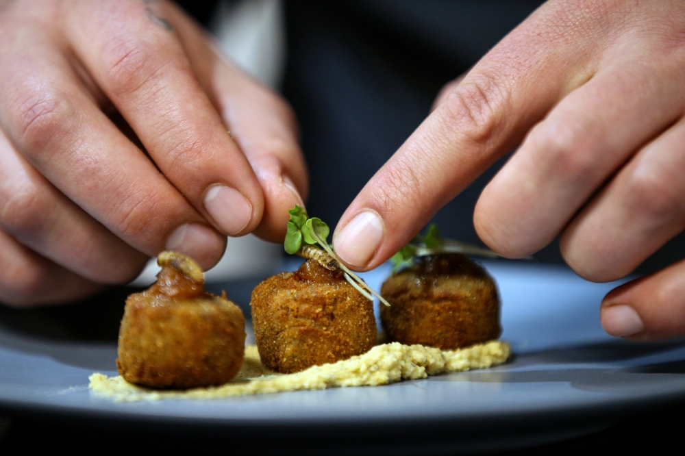 Chef Mario Barnard places coriander on croquettes made with Hermetia illucens (Black soldier fly larvae) flour and chickpea flour served on a bed of mopane worm tahini hummus at the Insect Experience Restaurant in Cape Town, South Africa, August 23, 2019.