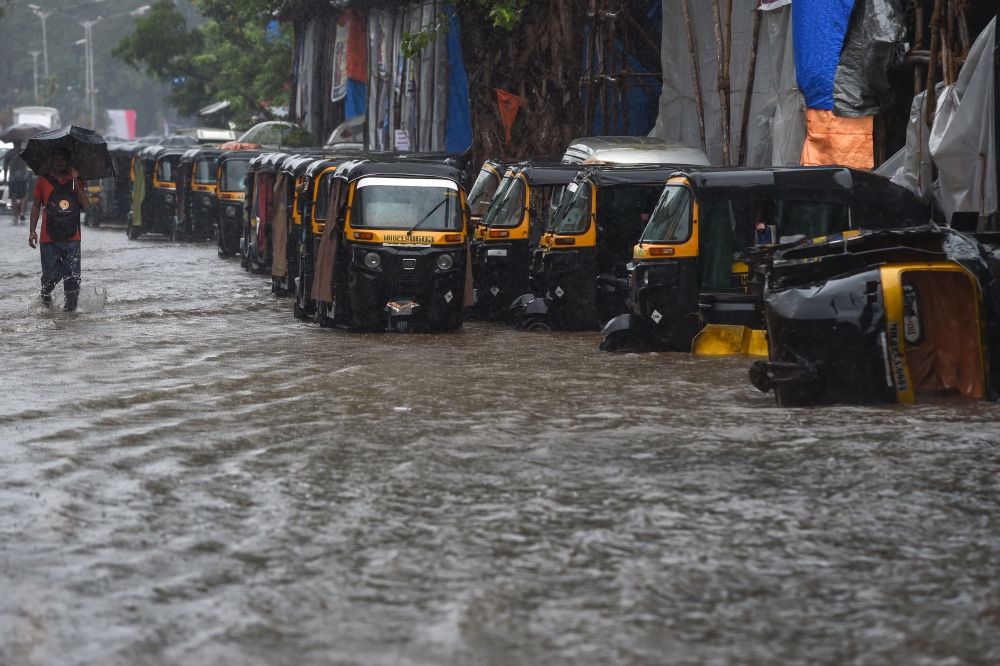 A pedestrian wades through a waterlogged street next to a line of auto rickshaws in heavy rain in Mumbai on September 4, 2019. / AFP / PUNIT PARANJPE