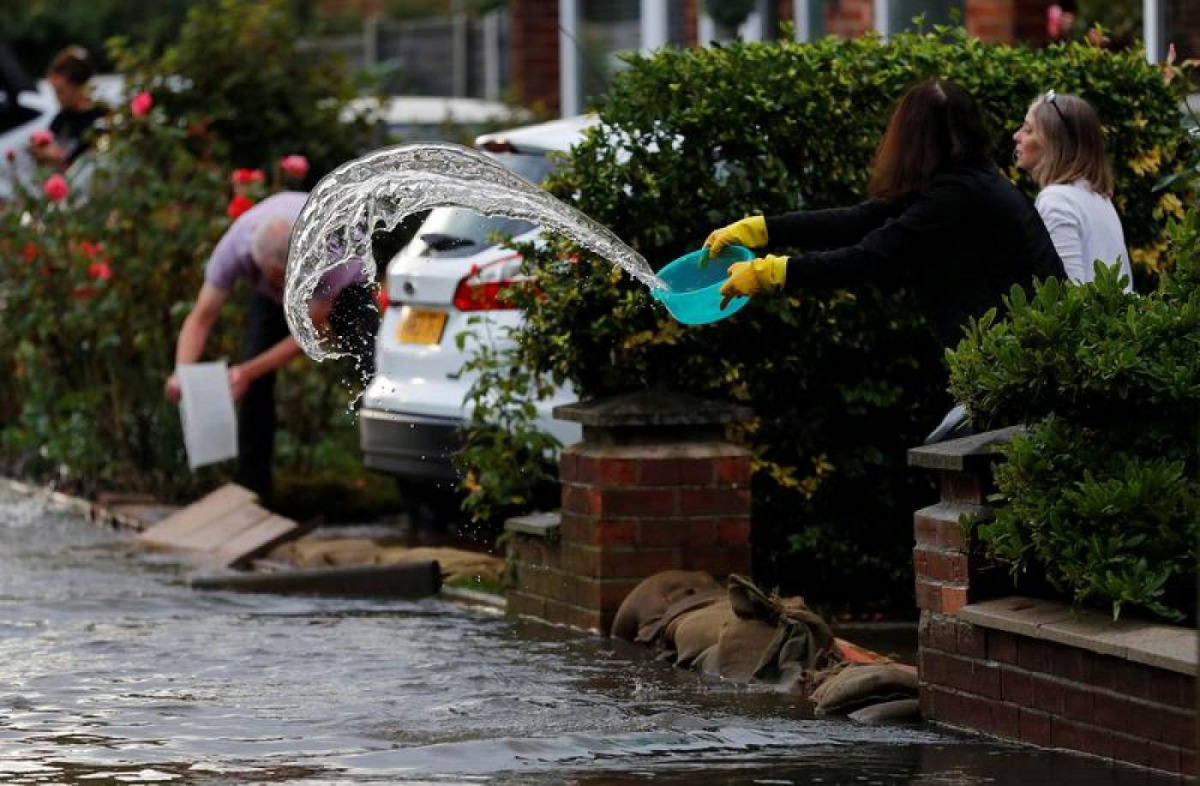 A woman uses a bowl to clear water from her drive to prevent rising flood water from entering her house in the Sale area of Manchester, Britain, July 31, 2019. Reuters/Phil Noble