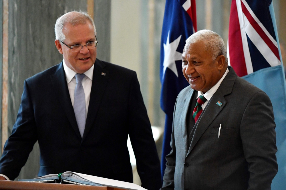 Australia's Prime Minister Scott Morrison (L) invites his Fijian counterpart Frank Bainimarama to sign a visitors book at Parliament House in Canberra on September 16, 2019.  / AFP / POOL / MICK TSIKAS 