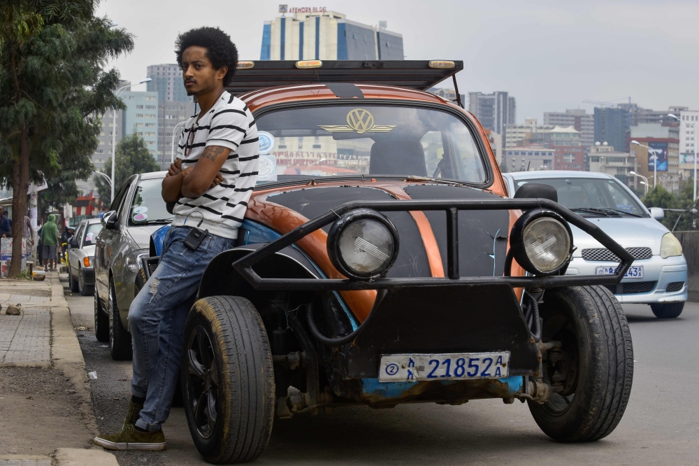 Ethiopian painter Robel Wolde, 25, poses in front of his Volkswagen Beetle during an interview with AFP, in Addis Ababa on September 2, 2019. AFP / Michael Tewelde