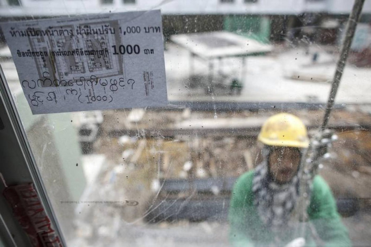 A multi-language sign, written the Thai, Cambodian and Myanmar languages, is seen as a construction labourer works at a building site in Bangkok June 18, 2014. Reuters/Athit Perawongmetha