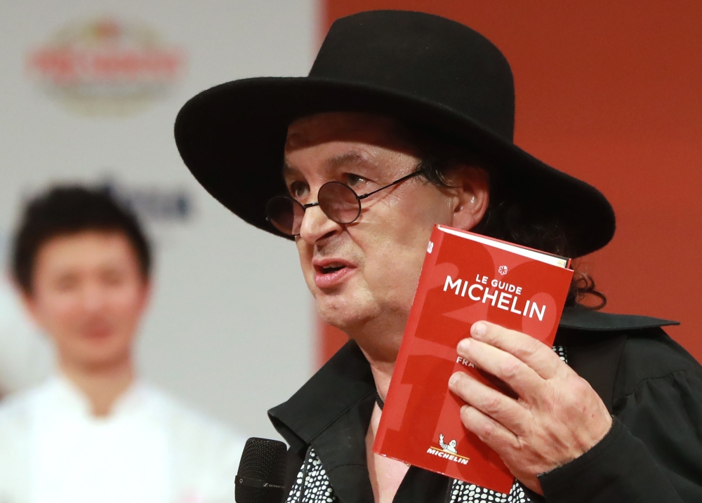 In this file photo taken on February 5, 2018 French chef Marc Veyrat, holds a Michelin guide after being awarded the maximum three Michelin stars, during the Michelin guide award ceremony at La Seine Musicale in Boulogne-Billancourt near Paris. / AFP / JA