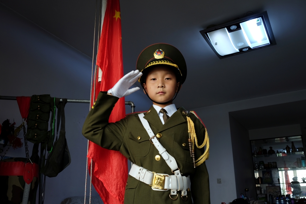 Feng Jianhan, 9, poses for a picture in military uniform next to a Chinese flag that he raises every morning through rope and pulley at his home in Xian, Shaanxi province, China September 26, 2019. Picture taken September 26, 2019. REUTERS/Irene Wang