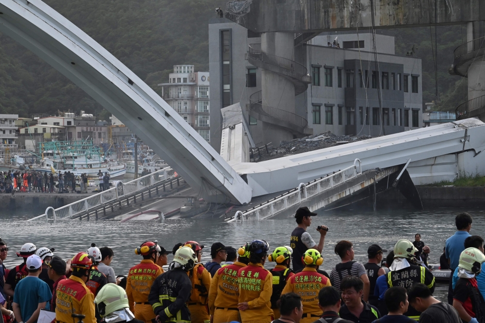 Rescue personnel look on at a bridge after it collapsed in the Nanfangao fish harbour in Suao township on October 1, 2019. The bridge collapsed in northeastern Taiwan on October 1 injuring at least 14 people as it smashed down onto fishing vessels moored 