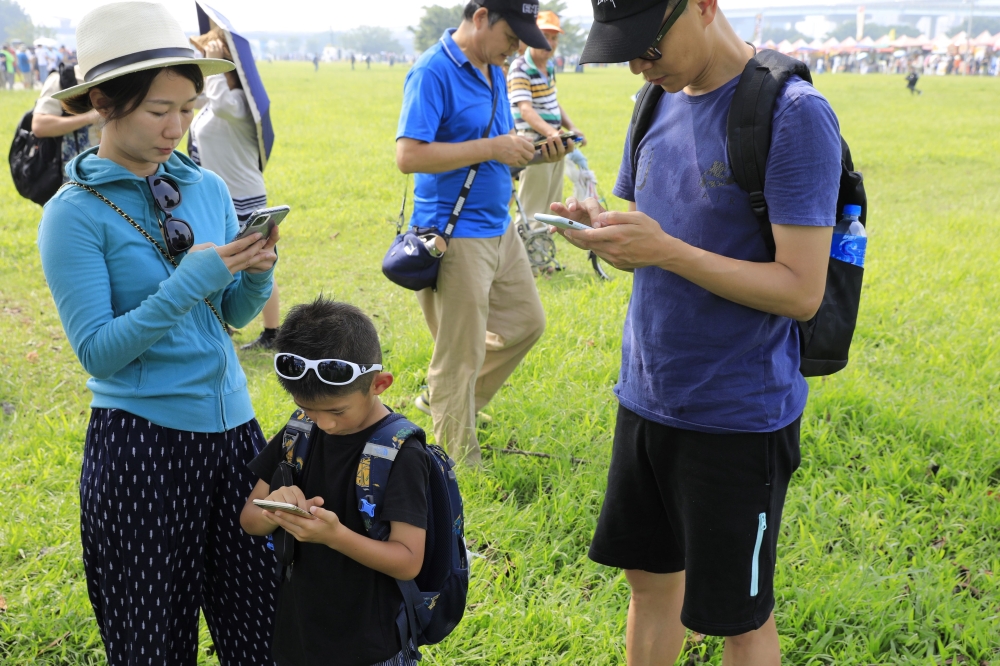 Visitors play Pokemon Go on their phones during the opening day of the Pokemon Go Safari Zone at the New Taipei Metropolitan Park in New Taipei City on October 3, 2019. / AFP / Daniel Shih