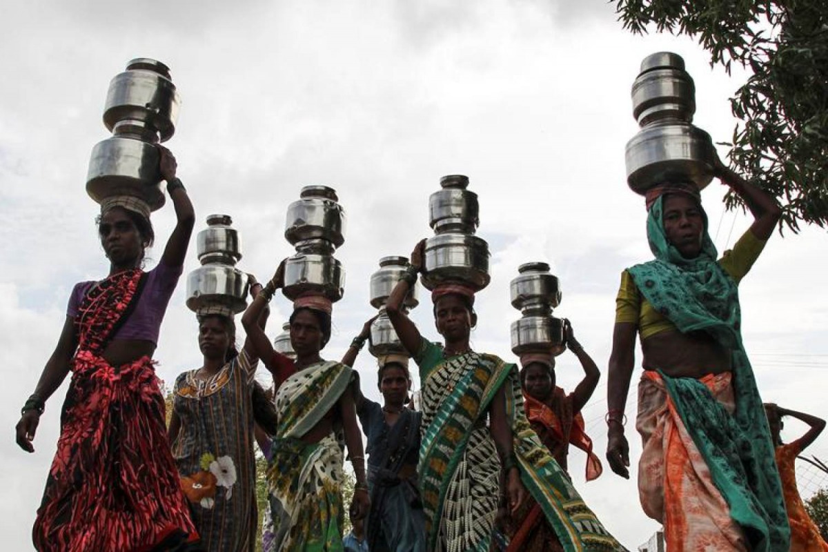 Women carry pitchers filled with water from an opening made to filter water next to a polluted lake in Thane, India June 13, 2019. Reuters/Prashant Waydande