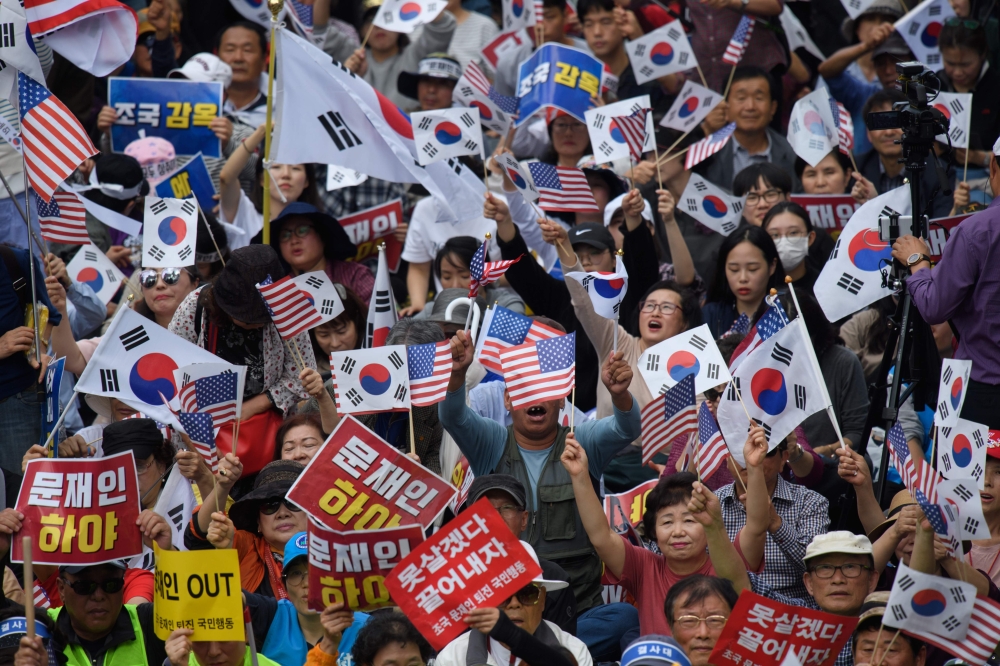 Anti-government protesters shout slogans and wave placards at a rally calling for president Moon Jae-in to step down, in central Seoul on October 3, 2019.   / AFP / Ed JONES