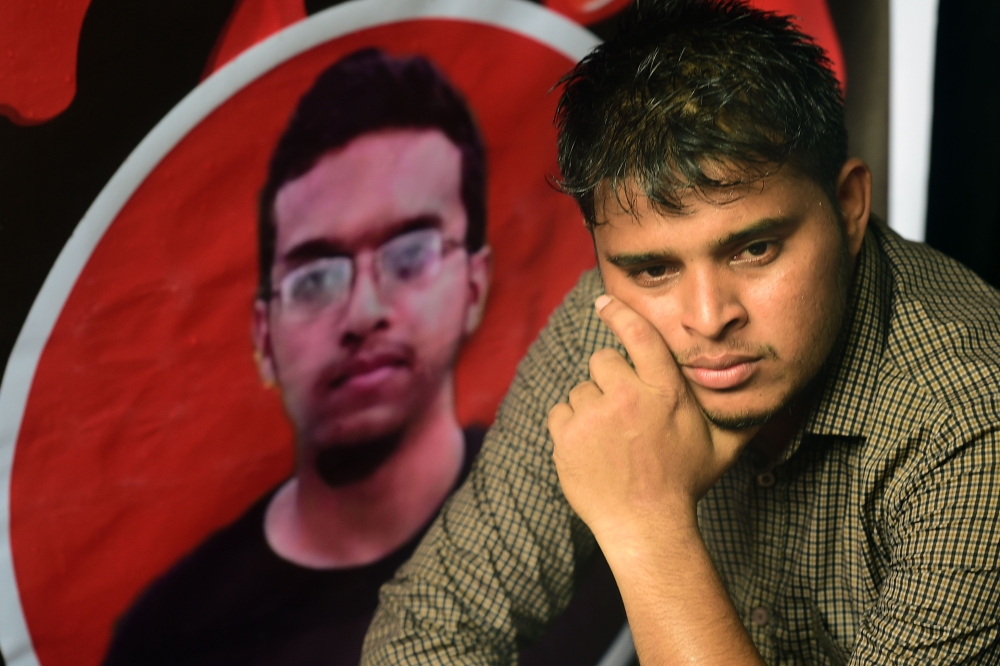 A Bangladeshi student sits during a protest in Dhaka on October 7, 2019, next to a portrait of Abrar Fahad, who was allegedly beaten to death by ruling party activists. AFP / Munir Uz Zaman 