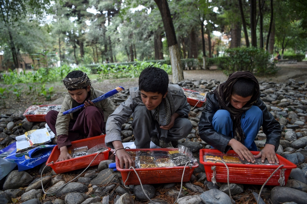 Young vendors Sabir (L), 11, Abdull Aziz (C), 12, and Tella Mohammad (R), 11, prepare dried fruits as they wait for customers at the Shahr-e-Naw Park in Kabul on October 6, 2019.  AFP / Wakil Kohsar



