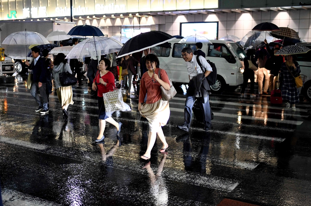 People use umbrellas to shelter from the rain as they cross a street next to the Shinjuku JR Tokyo Station on October 11, 2019. (AFP / FRANCK FIFE)