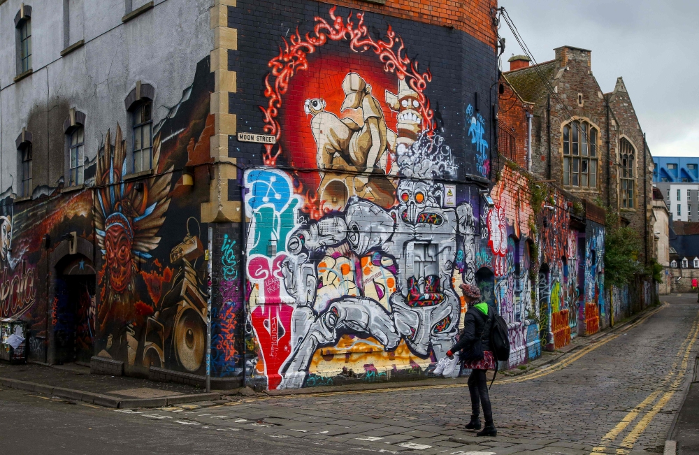A pedestrian walks past graffiti street art on the side of a building in Bristol on May 8, 2019. AFP / Geoff Caddick