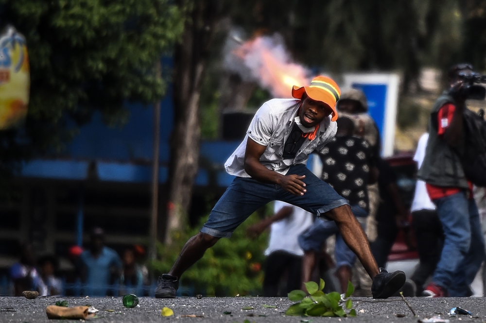 A protester runs for cover as police fire tear gas during a protest on the street to demand the resignation of the Haitian president in Port-au-Prince, Haiti on October 13, 2019. AFP / Chandan Khanna 