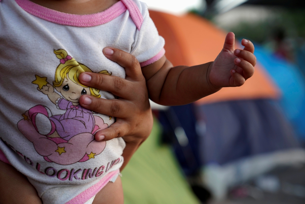 El Salvadoran asylum seeker Wendy, carries her eight-month-old daughter Pamela, in an encampment near the Gateway International Bridge where they have been living for about a month after they were sent back under the 