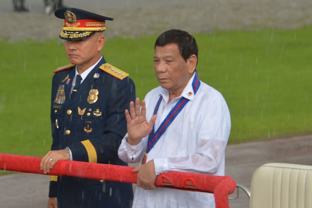 This file photo taken on August 8, 2018 shows Philippine President Rodrigo Duterte (R) reviewing policemen along with national police chief Oscar Albayalde (L) in a sudden downpour during the 117th police anniversary celebration at the national headquarte