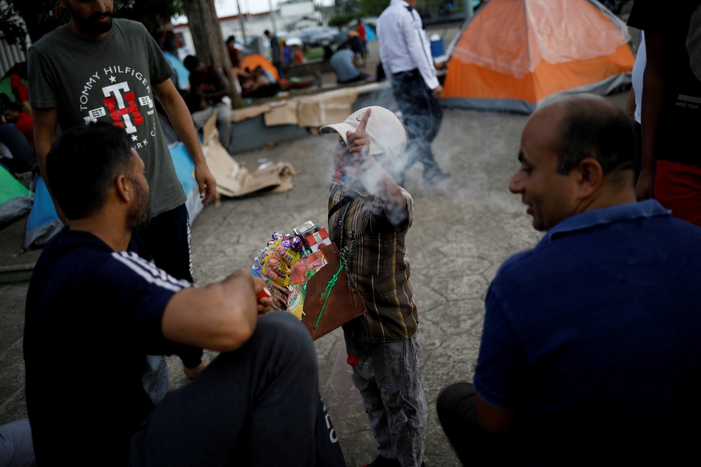 A boy selling candies and cigarettes gestures to the camera as he argues with migrants from India outside of Siglo XXI migration facility in Tapachula, Mexico, May 13, 2019. REUTERS/Andres Martinez Casares/File Photo