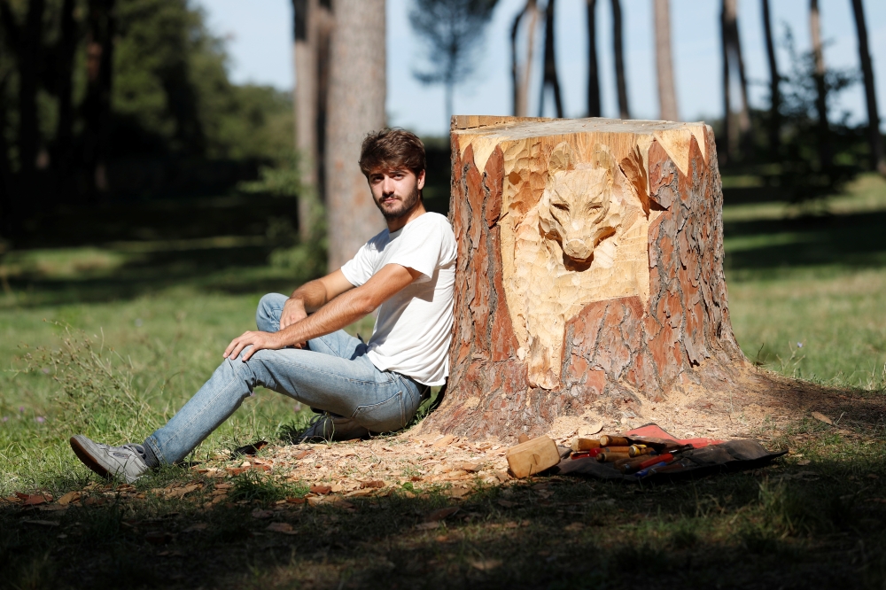 Sculptor Andrea Gandini is pictured next a sculpture of a wolf's face from a dead tree stump in the Villa Pamphili park, Rome, Italy, October 18, 2019. Picture taken October 18, 2019 REUTERS/Remo Casilli