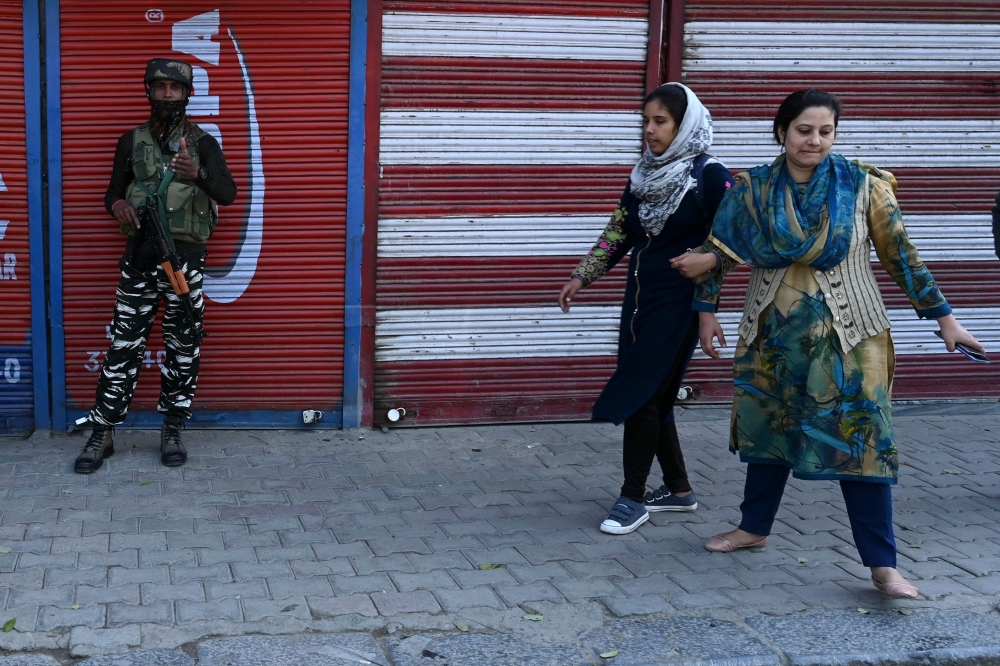 An Indian paramilitary trooper gestures as Kashmiri women walk past next to closed shops during a lockdown in Srinagar on October 23, 2019.  AFP / Tauseef Mustafa
 