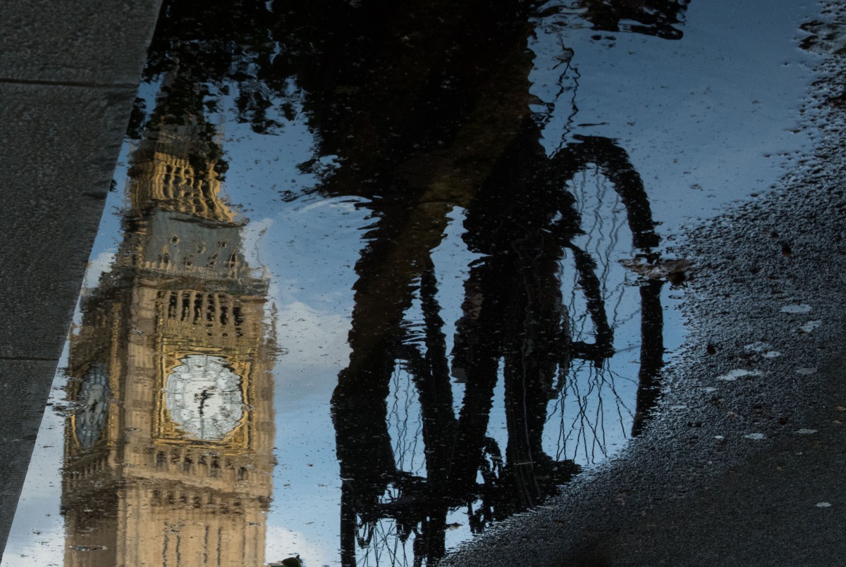 Big Ben is reflected in a puddle as a cyclist rides by in London on  June 27, 2016. AFP/ Leon Neal 