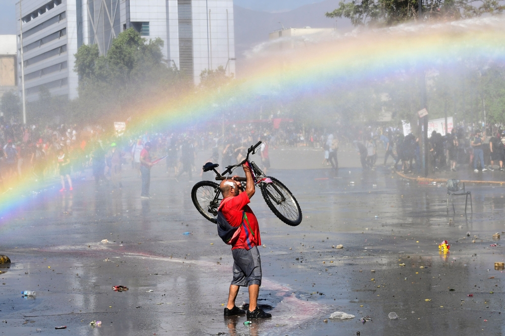 A demonstrator lifts his bike in the air during clashes with riot police in Santiago on October 24, 2019. AFP / Martin Bernetti