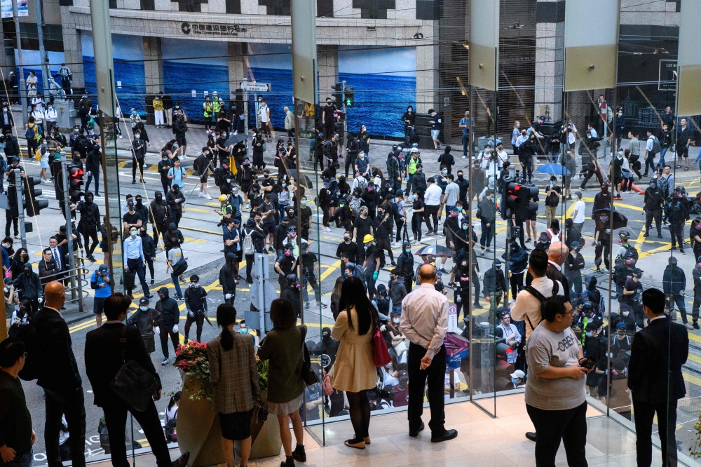 Bystanders (foreground) watch from a shopping mall as protesters (back) gather on a road below in Hong Kong's Central district on November 11, 2019.  AFP / Anthony Wallace 