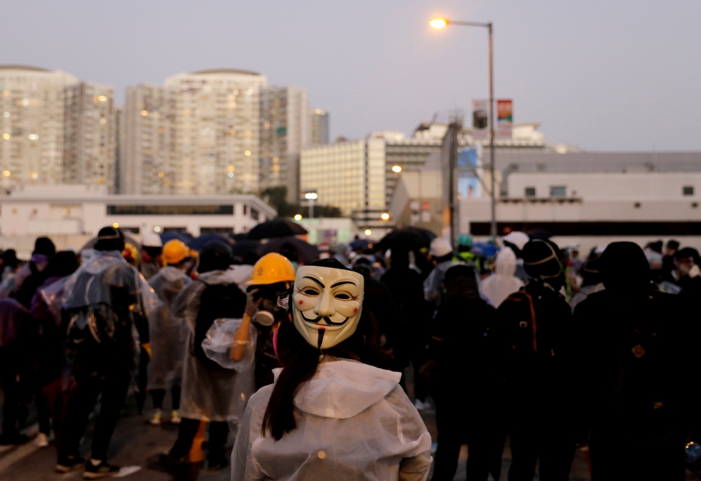 A protester wearing a Guy Fawkes mask stands on the bridge above the Cross Harbour Tunnel during clashes with police outside Hong Kong Polytechnic University (PolyU) in Hong Kong, China November 17, 2019. Reuters/Adnan Abidi