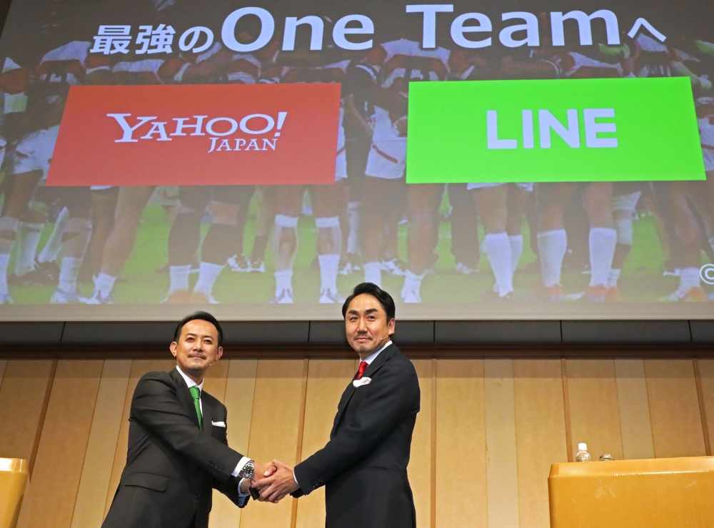 Kentaro Kawabe (L), CEO and president of Z Holdings and Takeshi Idezawa (R), CEO and president of LINE shake hands during a joint press conference in Tokyo on November 18, 2019. Japan's Z Holdings, formerly Yahoo Japan, will merge with mobile chat app ope
