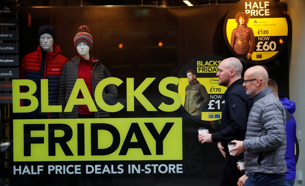 People walk past a sign advertising Black Friday offers in the window of a Blacks outdoor clothing store in Manchester, Britain, November 22, 2019. Reuters/Phil Noble