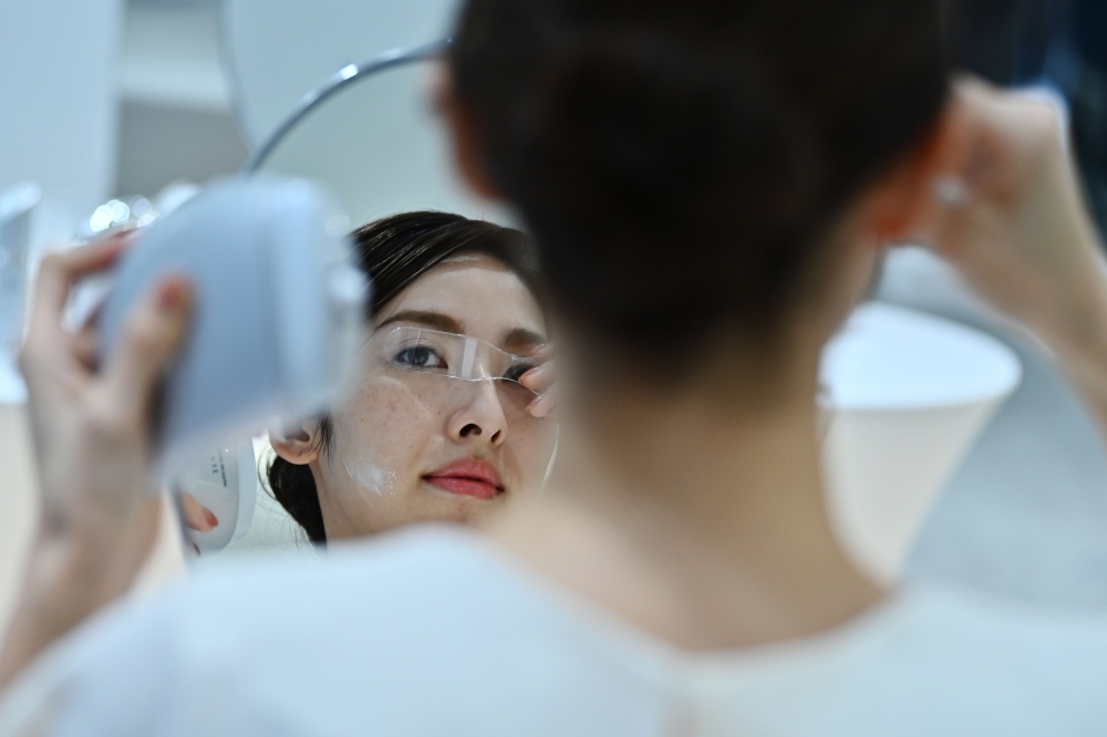 An employee for Japanese cosmetics company Kao uses a palm-sized diffuser on her face, during a product demonstration in Tokyo on December 4, 2019. AFP / CHARLY TRIBALLEAU
