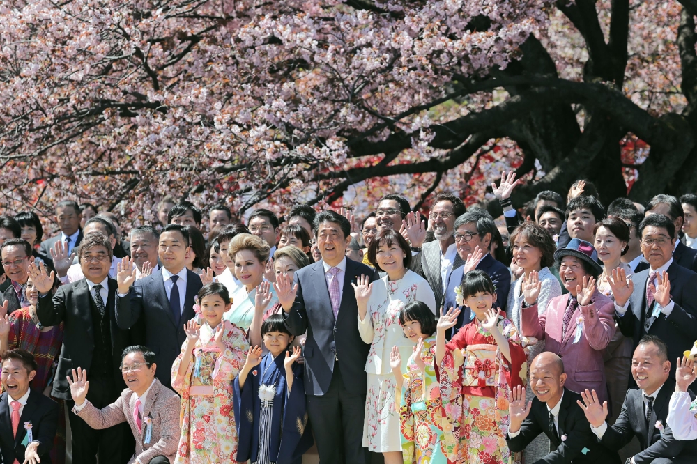 In this file photo taken on April 13, 2019, Japanese Prime Minister Shinzo Abe (centre L) and his wife Akie (center R) pose for pictures with their guests during his cherry blossom viewing party at a park in Tokyo. - Japan OUT / AFP / JIJI PRESS / STR 