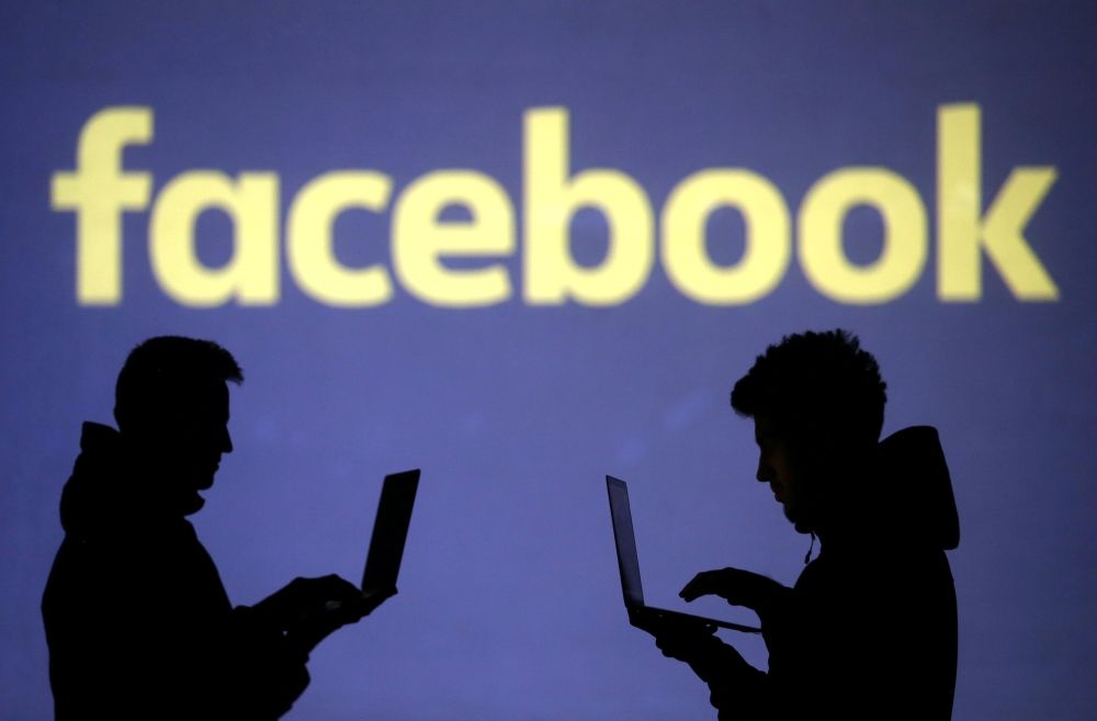 Silhouettes of laptop users are seen next to a screen projection of Facebook logo in this picture illustration, March 28, 2018. Reuters / Dado Ruvic