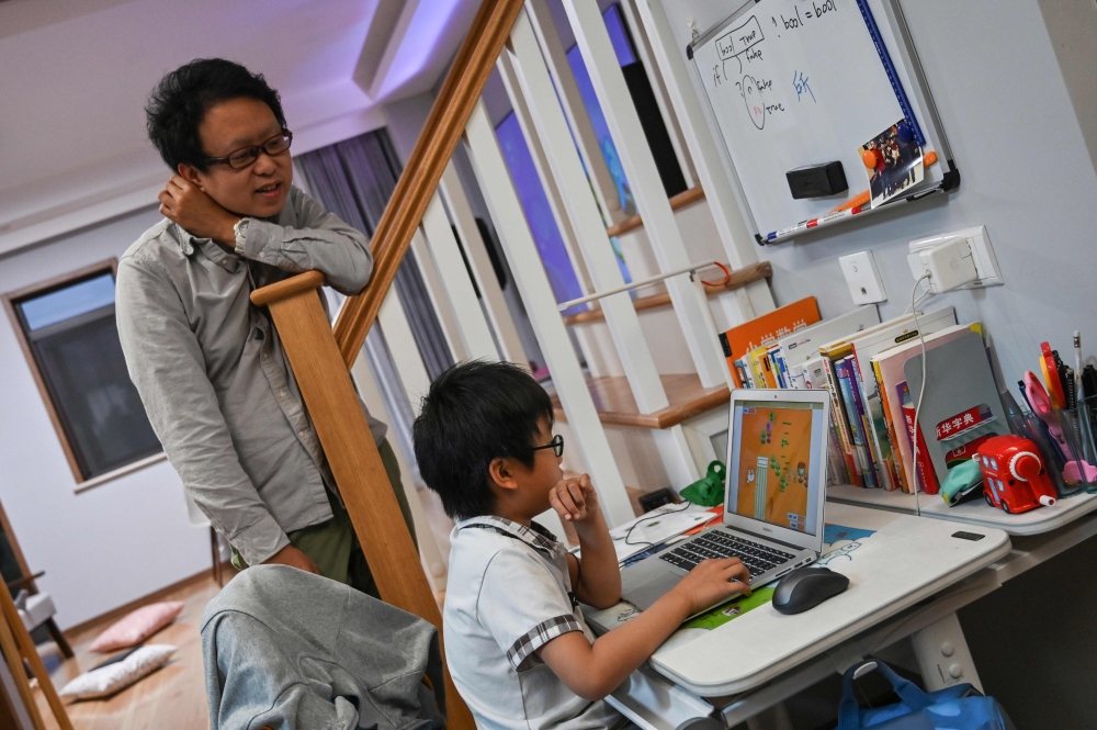 This photo taken on November 7, 2019 shows Zhou Ziheng (L) helping his son Vita to create a game with coding on his laptop at their home in Shanghai. AFP / Hector Retamal