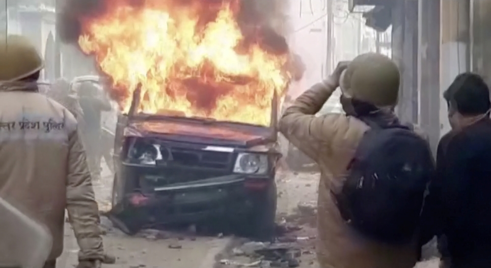 Police personnel look at a burning vehicle during clashes over citizenship law in Bulandshahar, Uttar Pradesh, India December 20, 2019 in this still image taken from a video. 