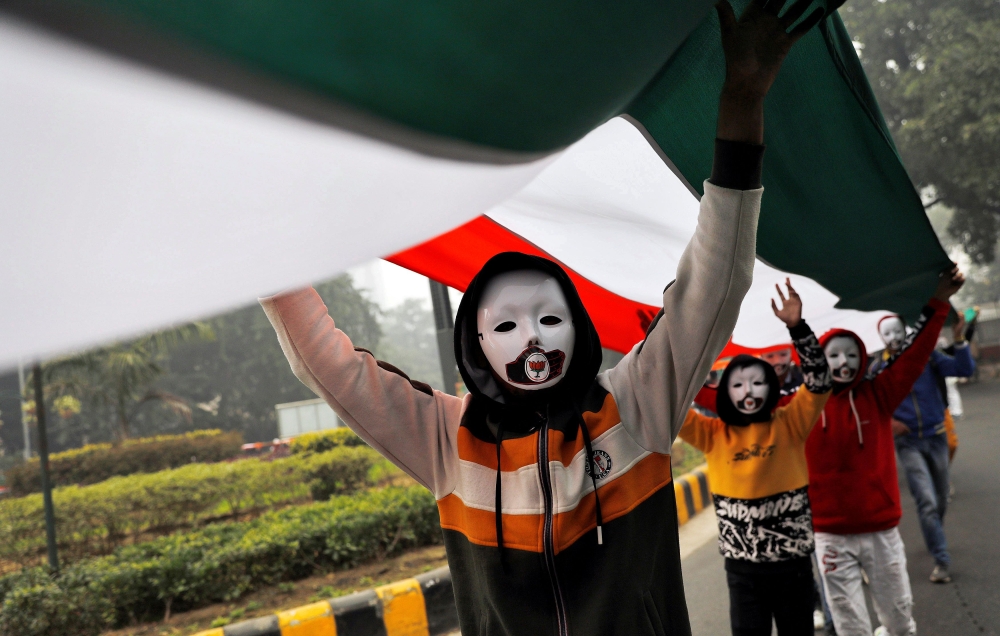 Demonstrators wearing masks hold a tricoloured flag in front of the India Gate during a demonstration against what they say was an alleged police action conducted during recent protests against a new citizenship law, in New Delhi, India, December 30, 2019