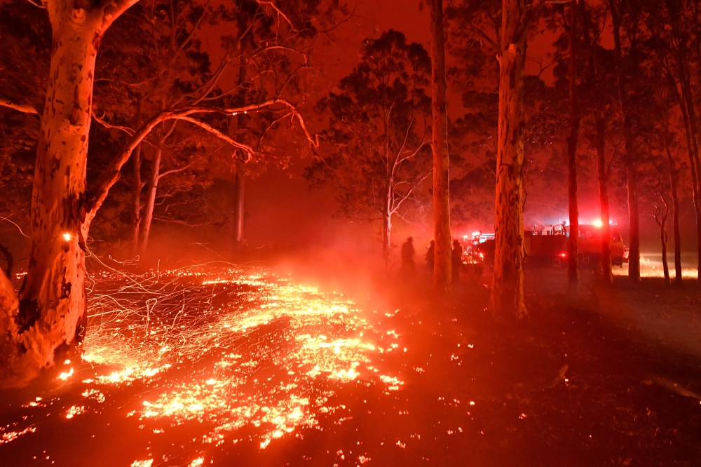 :Burning embers cover the ground as firefighters (back R) battle against bushfires around the town of Nowra in the Australian state of New South Wales on December 31, 2019. / AFP / Saeed KHAN 