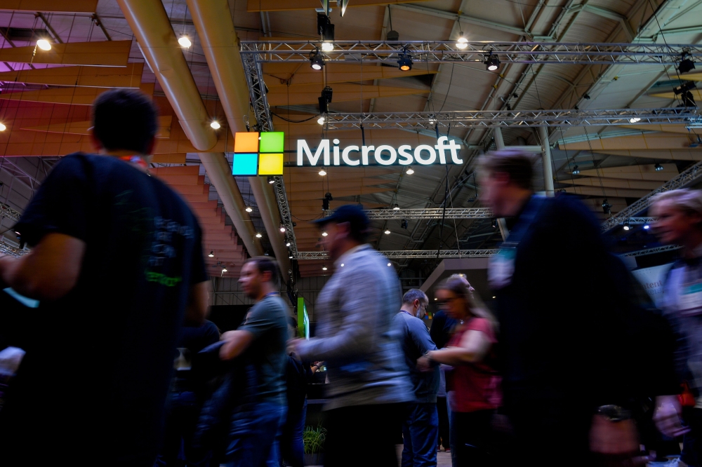 In this file photo taken on November 6, 2019 Attendees walk past the logo of US multinational technology company Microsoft during the Web Summit in Lisbon. / AFP / AFP / PATRICIA DE MELO MOREIRA