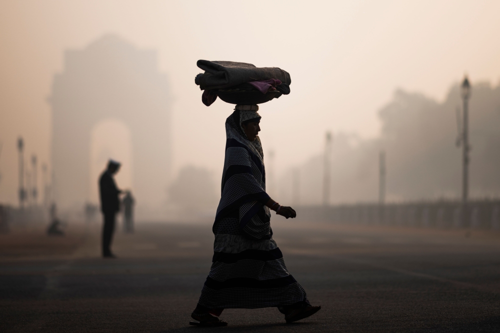 A woman balances a load on her head as she crosses a street near India Gate in heavy smoggy conditions in New Delhi on December 6, 2019. AFP / Jewel Samad