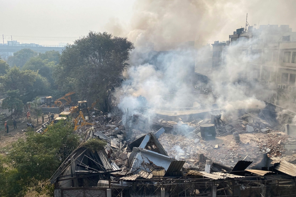  Smoke rises over the debris of a building that collapsed, as rescue workers (L) gather nearby, in New Delhi on January 2, 2020. / AFP / Atish PATEL