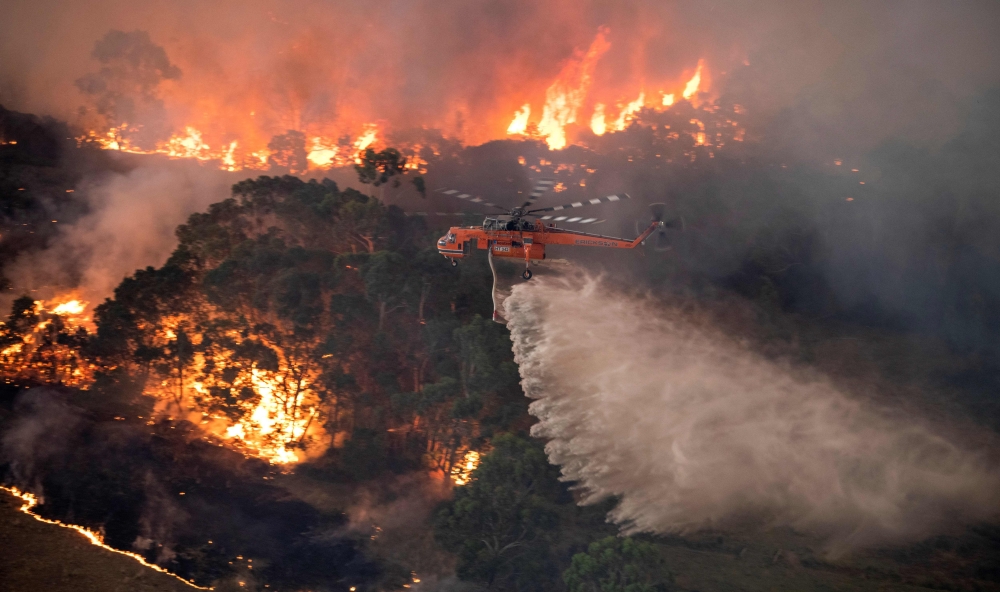 A handout photo taken and received on December 31, 2019 from the State Government of Victoria shows a helicopter fighting a bushfire near Bairnsdale in Victoria's East Gippsland region.  