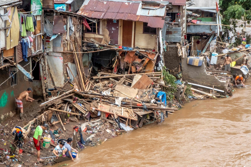 Indonesians clean their homes and cutlery along the river in Jakarta on January 3, 2020, after flooding triggered by heavy rain which started on New Year's Eve hit the area. / AFP / BAY ISMOYO 