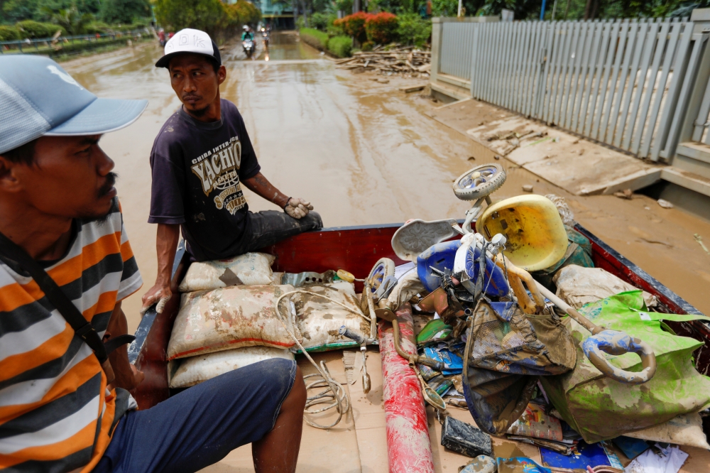 Men collecting damaged items ride on the back of a car through the mud, at a residential area affected by floods in Bekasi, West Java province, Indonesia, January 3, 2020. REUTERS/Willy Kurniawan