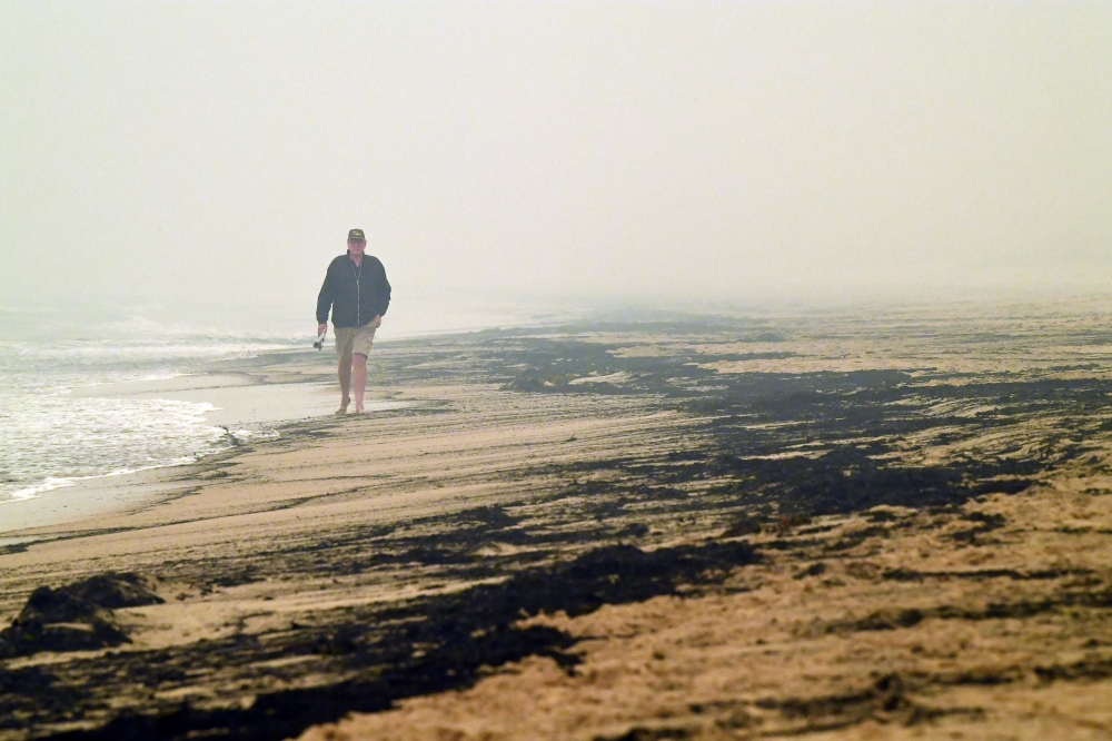Local resident Dave Iredale walks past ash from bushfires washed up on a beach in Merimbula, in Australia's New South Wales state on January 5, 2020. Australians on January 5 counted the cost from a day of catastrophic bushfires that caused 
