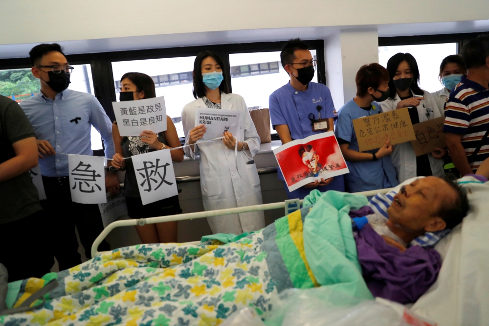 FILE PHOTO: A patient is wheeled past as healthcare staff hold posters in a human chain to protest against police brutality at Queen Mary Hospital, in Hong Kong, September 2, 2019. Reuters / Anushree Fadnavis