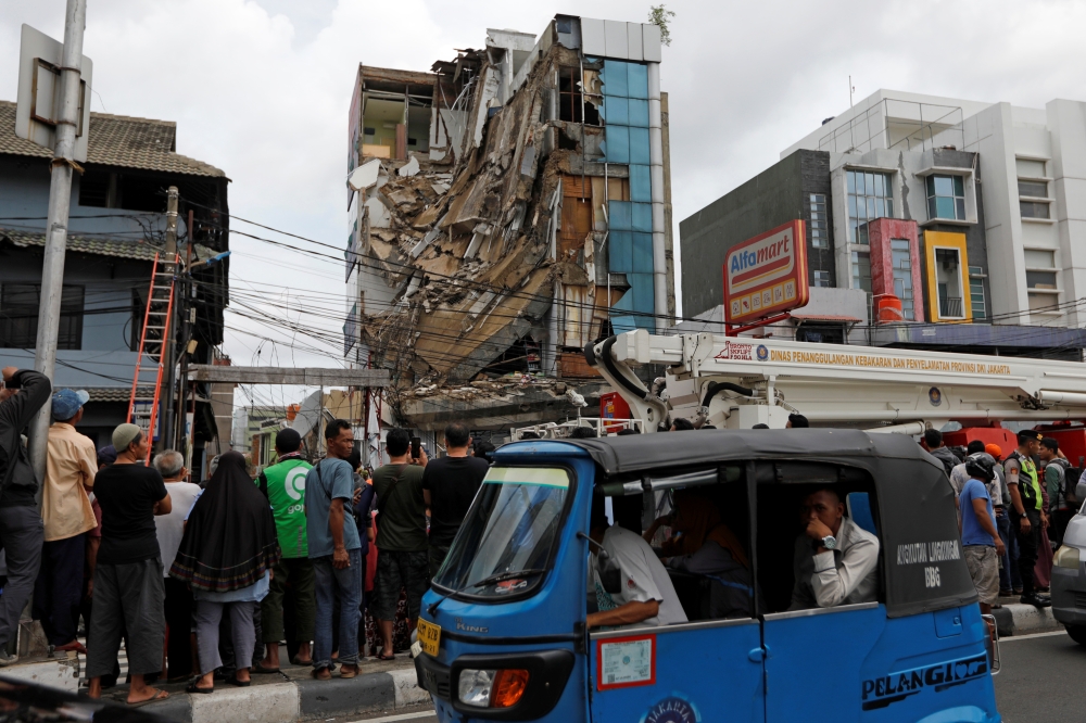 People in a three-wheeler pass a partially-collapsed building in Jakarta, Indonesia, January 6, 2020. REUTERS/Willy Kurniawan
