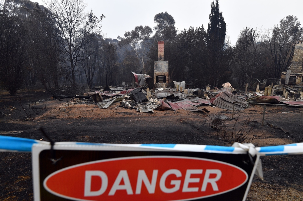 A woodchip mill burnt by bushfires is seen as smoke rises in Eden in Australia's New South Wales state on January 6, 2020. Reserve troops were deployed to fire-ravaged regions across three Australian states on January 6 after a torrid weekend that turned 