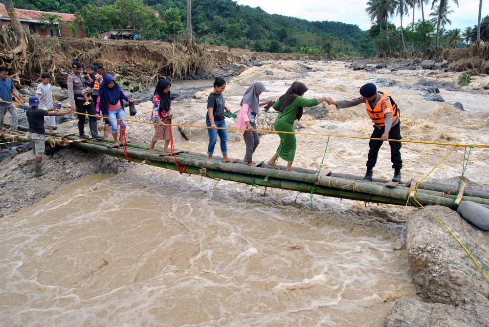 Police officers help people to get through an emergency bridge over the Cidurian river in Bogor, Indonesia, January 3, 2020 in this photo taken by Antara Foto. Antara Foto/Arif Firmansyah/ via REUTERS
