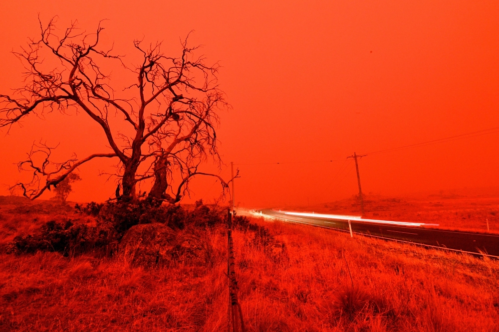 TOPSHOT - A long exposure picture shows a car commuting on a road as the sky turns red from smoke of the Snowy Valley bushfire on the outskirts of Cooma on January 4, 2020. Up to 3,000 military reservists were called up to tackle Australia's relentless bu