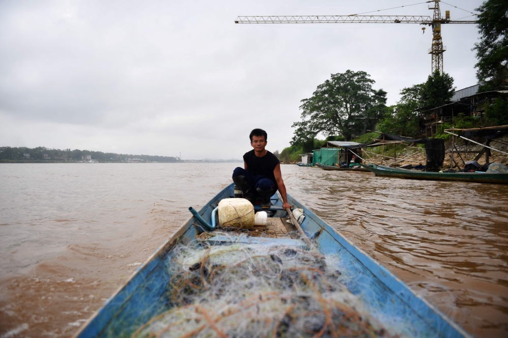Fisherman Kome Wilai fishing from his boat along the Mekong River between Chiang Rai province in Thailand (R) and Laos (L) on September 20, 2019. AFP / Lillian Suwanrumpha